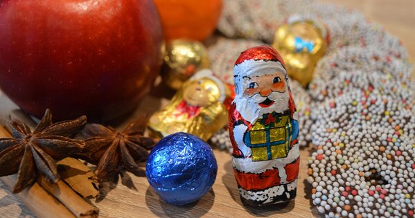 Ausschnitt eines Tisches mit Äpfeln, Mandarinen, Sternanis, einer blauen Schokokugel, einem Schokoweihnachtsmann, kleinen Schokofiguren und Schokokränzen.