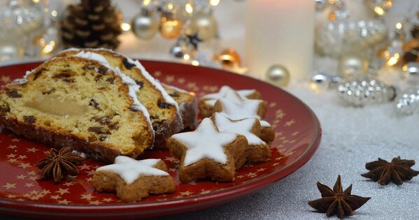 Ein heller weihnachtlich dekorierter Tisch, im Fokus ein roter Teller mit einem Stollen, Zimtsternen und Sternanis.