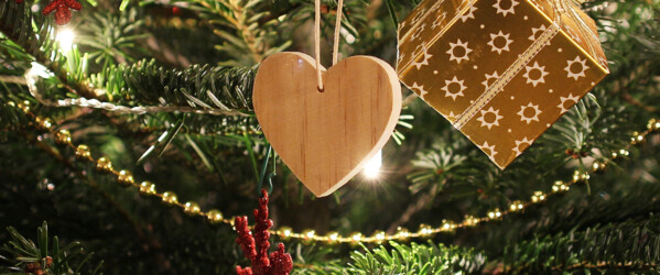 Ausschnitt eines geschmückten Tannenbaumes mit Anhängern, ein Holzherz, ein Geschenk, Kugeln und einer Perlengirlande